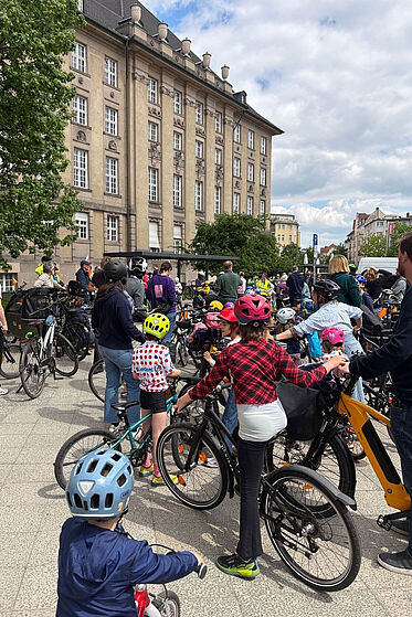 Mehrere Erwachsene und Kinder mit Fahrrad sammeln sich an einem Treffpunkt