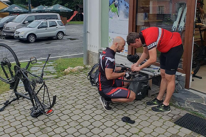 Zwei Männer beugen sich über einen abmontierten Fahrradreifen und reparieren etwas.