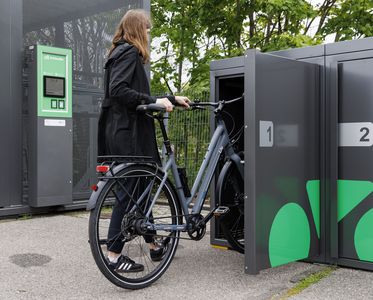 Eine Frau stell ihr Fahrrad in eine Fahrradbox.