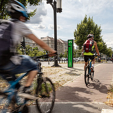 Fahrradfahrer auf Radweg kurz vor einem grünen Fahrradbarometer