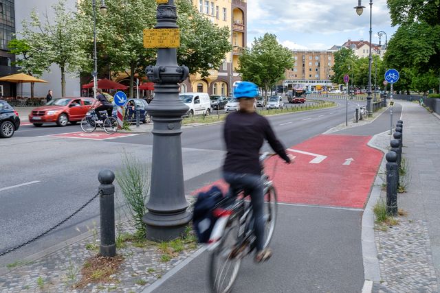 Fahrradfahrer fährt auf einem Hochbordradweg, der im Kreuzungsbereich rot markiert ist.