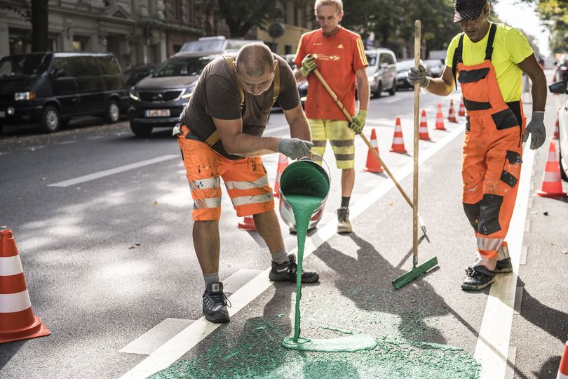 Bauarbeiter verteilen grüne Farbe auf einem Radweg