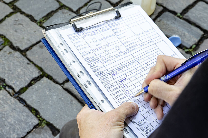 Eine Person trägt Messergebnisse in ein Formular an einem Klemmbrett ein.