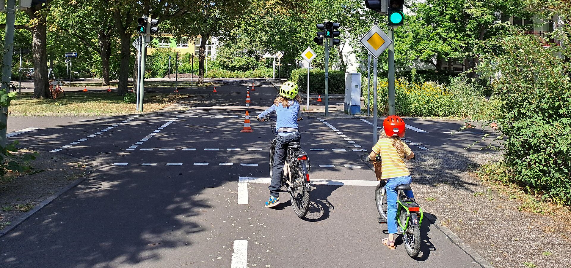 zwei Kinder sind von hinten zu sehen, wie sie auf einer Straße einer Jugendverkehrsschule mit Fahrrädern fahren