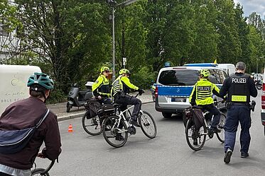 Polizisten auf Fahrrädern fahren hinter einem Polizeiauto