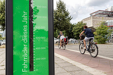 Fahrradbarometer im Vordergrund, dahinter fahren Radfahrer auf einem Fahrradweg