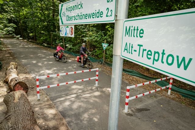 Radwegweiser mit der Aufschrift "Mitte", "Alt-Treptow", im Hintergrund Radfahrer