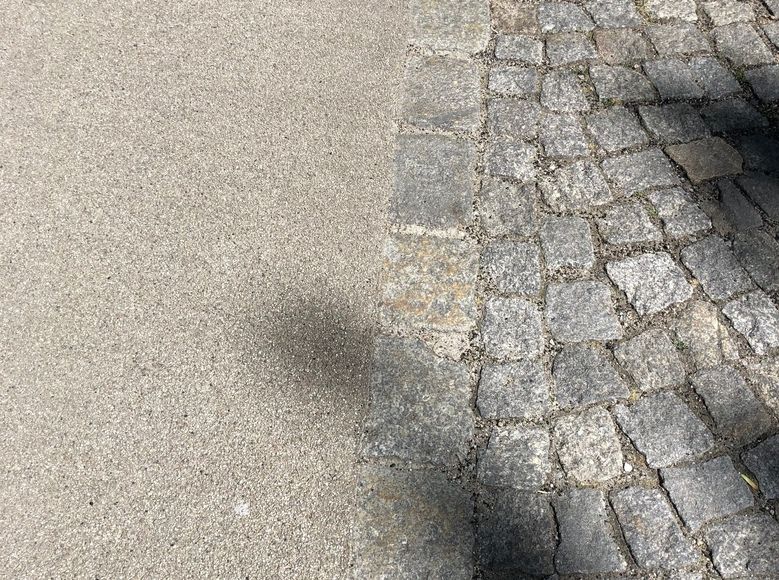Nahaufnahme von einem Wegebelag, Asphalt und Kopfsteinpflaster nebeneinander