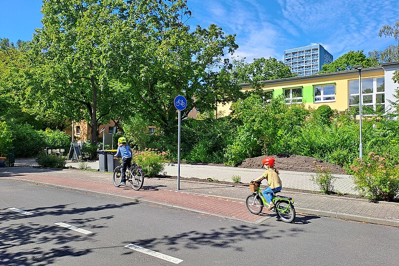 zwei Kinder sind von der Seite zu sehen, wie sie auf einen Radweg einer Jugendverkehrsschule Fahrrad fahren