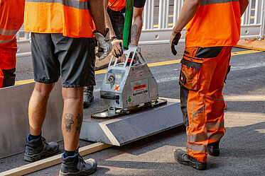 Mehrere Bauarbeiten in orangener Arbeitskleidung bauen Betonborde an einem Radfahrstreifen ein.
