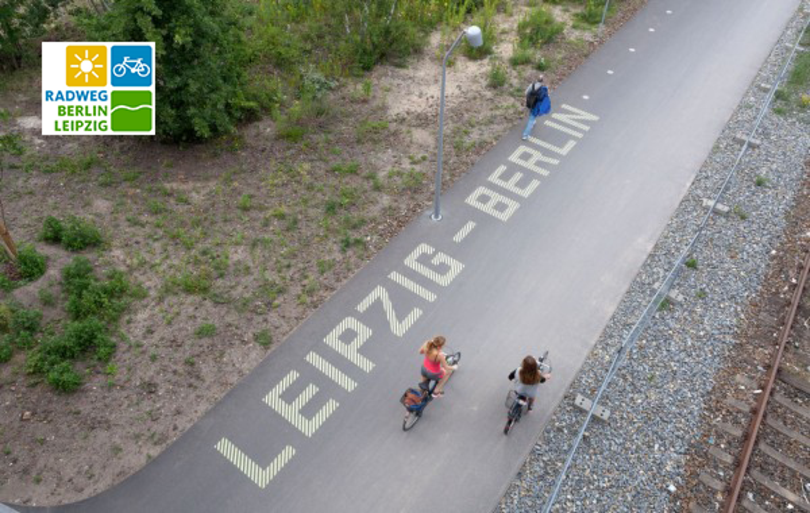 Radfahrer von oben auf einen asphaltierten Weg, auf dem in weißer Farbe geschrieben steht: "Leipzig - Berlin"