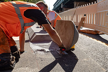 Ein Bauarbeiter befestigt ein Beton-Bord neben einem Radfahrstreifen.