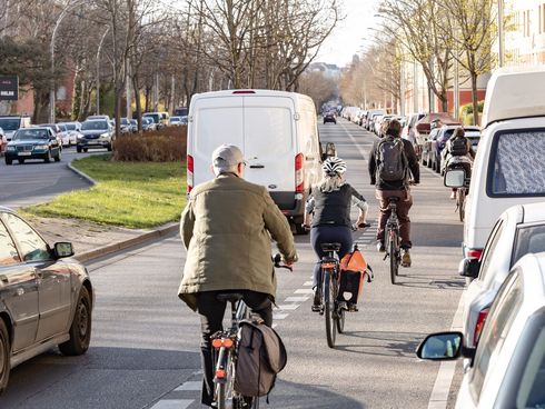 Fahrradfahrer fahren auf einem Schutzstreifen zwischen der Fahrbahn und geparkten Autos