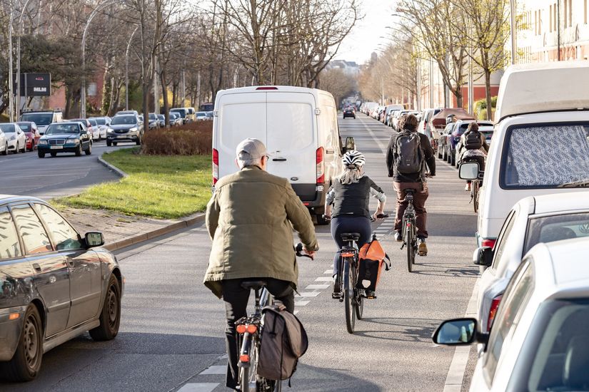 Fahrradfahrer fahren auf einem Schutzstreifen zwischen der Fahrbahn und geparkten Autos