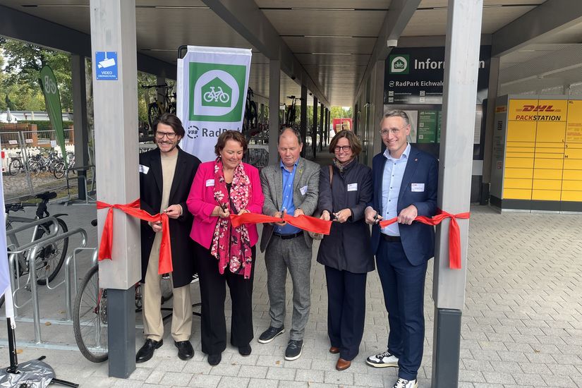 Fünf Personen durchschneiden ein rotes Band und eröffnen ein Fahrradparkhaus