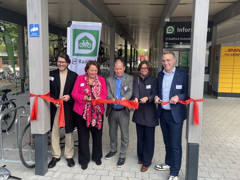 Fünf Personen durchschneiden ein rotes Band und eröffnen ein Fahrradparkhaus