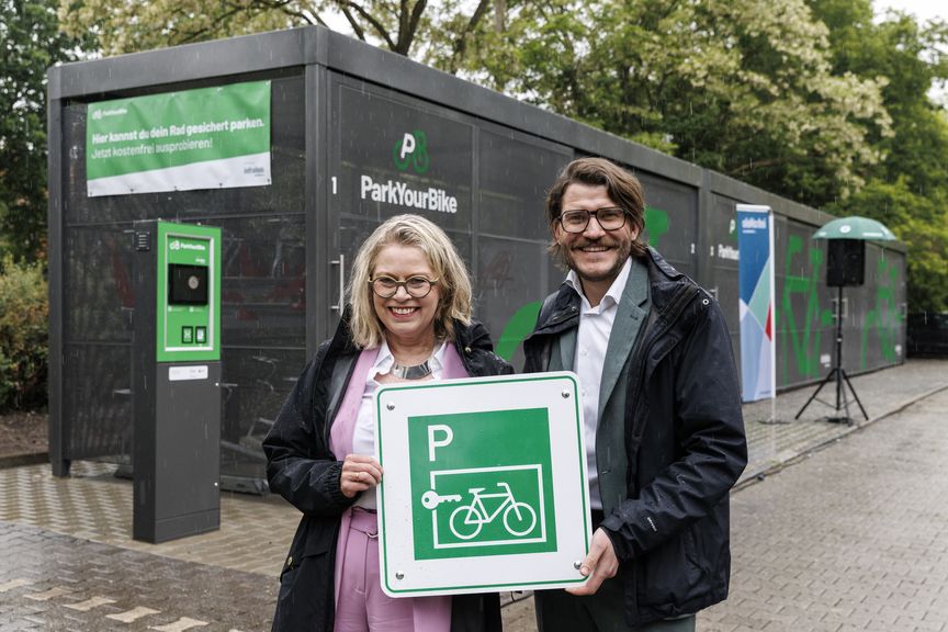 Verkehrssenatorin Ute Bonde und infraVelo-Geschäftsführer Michael Fugel halten Fahrradparken-Schild hoch vor Abstellanlage