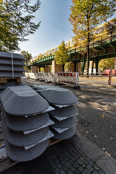 Mehrere Protektions-Borde aus Beton lagern am Straßenrand einer Baustelle auf einer Palette.