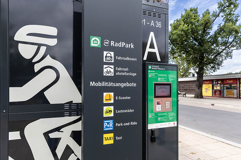 Terminal einer gesicherten Fahrradabstellanlage, daneben ein Hinweisschild mit Piktogrammen für E-Scooter, Lastenräder, Taxi und Park+Ride