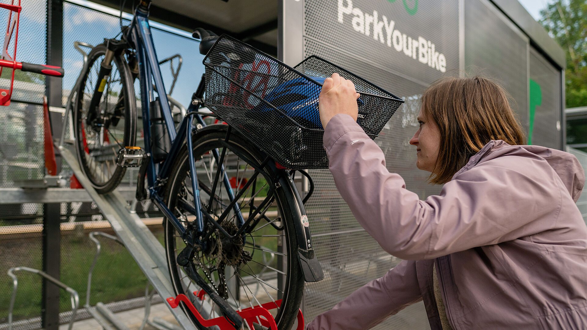 eine Frau parkt ihr Fahrrad in der oberen Etage einer Sammelschließanlage