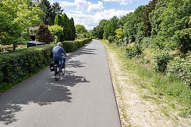 Fahrradfahrer fährt auf asphaltiertem Weg neben Kleingärten