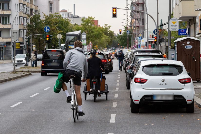 Fahrradfahrer fahren auf der Grunewaldstraße auf eine Kreuzung zu. Rechts von ihnen parken Autos.