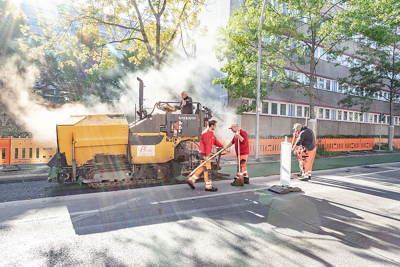 Ein Baufahrzeug verteilt grün eingefärbten Asphalt auf der Fahrbahn.