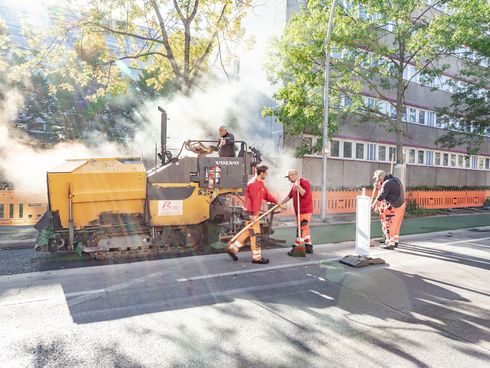 Ein Baufahrzeug verteilt grün eingefärbten Asphalt auf der Fahrbahn.