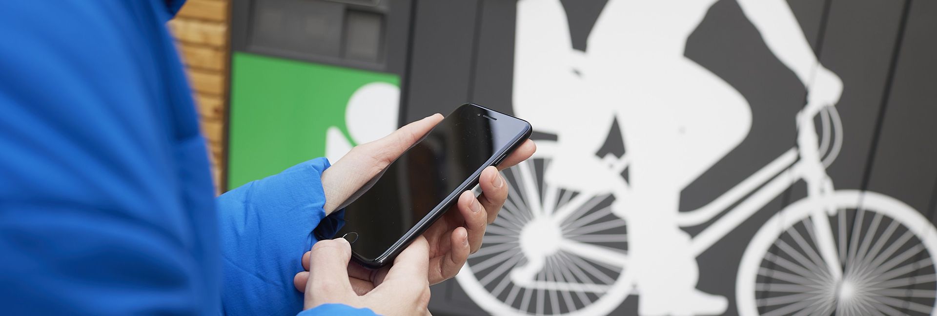 Nahaufnahme von Händen, die ein Smartphone halten, vor einer Abstellanlage