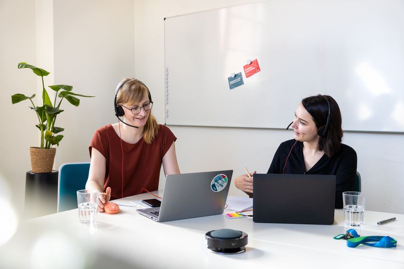 Zwei Frauen mit Laptops an einem Besprechungstisch