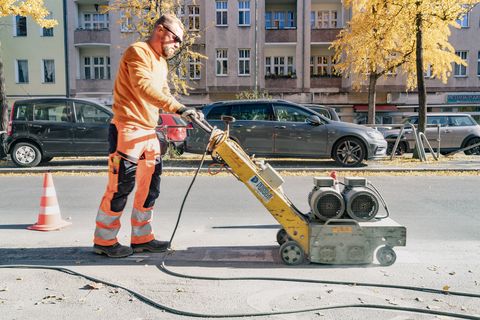 Bauarbeiter sind damit beschäftigt, auf der Richard-Wagner-Straße in Charlottenburg die vorhandenen Fahrbahnmarkierungen zu entfernen um anschließend eine Grünbeschichtung auf den Radweg aufzubringen.