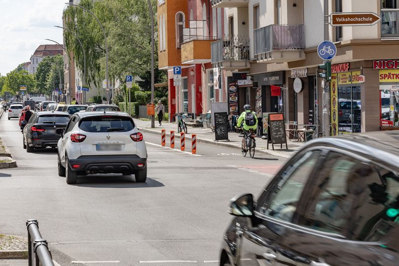 Stadtstraße mit Autoverkehr, im Hintergrund geschützter Radfahrstreifen und Geschäfte