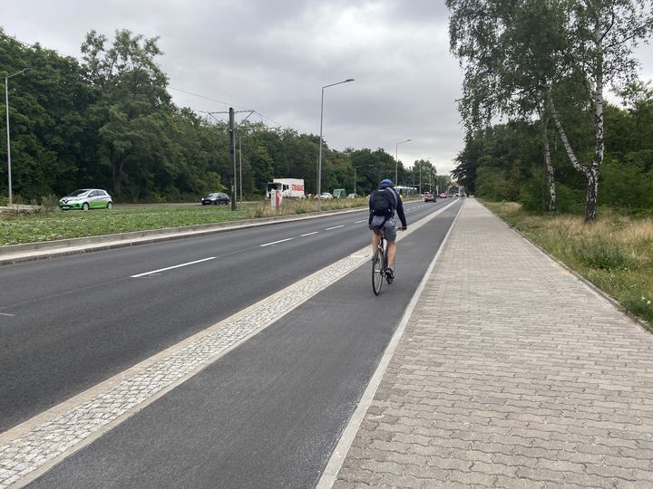 Radfahrer fährt auf einem Hochbordradweg rechts neben der Straße