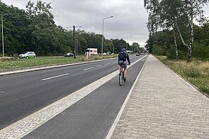 Radfahrer fährt auf einem Hochbordradweg rechts neben der Straße
