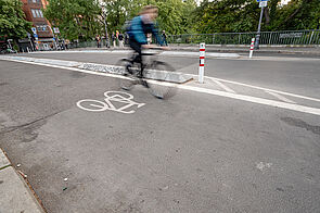 Radfahrende auf einem durch Betonborde geschützten Radweg auf der Hobrechtbrücke.