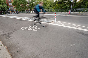 Radfahrende auf einem durch Betonborde geschützten Radweg auf der Hobrechtbrücke.