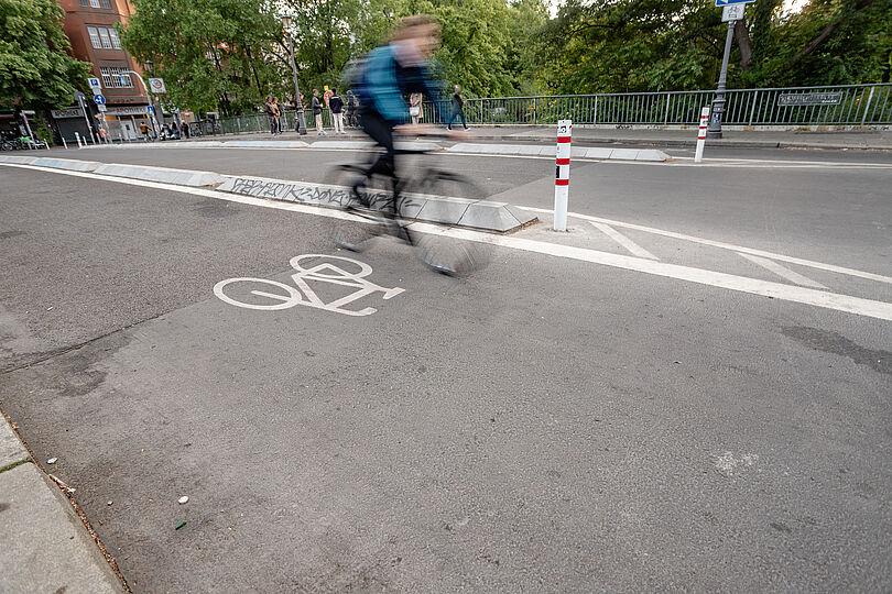 Radfahrende auf einem durch Betonborde geschützten Radweg auf der Hobrechtbrücke.