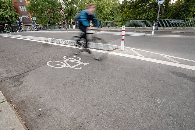 Radfahrende auf einem durch Betonborde geschützten Radweg auf der Hobrechtbrücke.