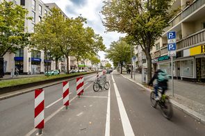 geschützter Radfahrstreifen am rechten Fahrbahnrand, links davon Sperrflächen und Abstellbügel für Fahrräder
