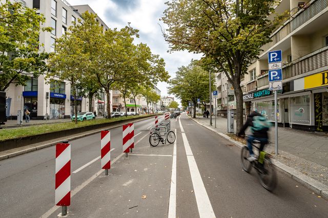 geschützter Radfahrstreifen am rechten Fahrbahnrand, links davon Sperrflächen und Abstellbügel für Fahrräder
