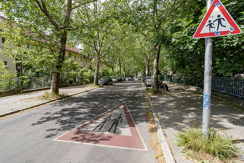 Asphaltierter Straße mit einem auf dem Boden markierten Gefahrenzeichen "Kinder".
