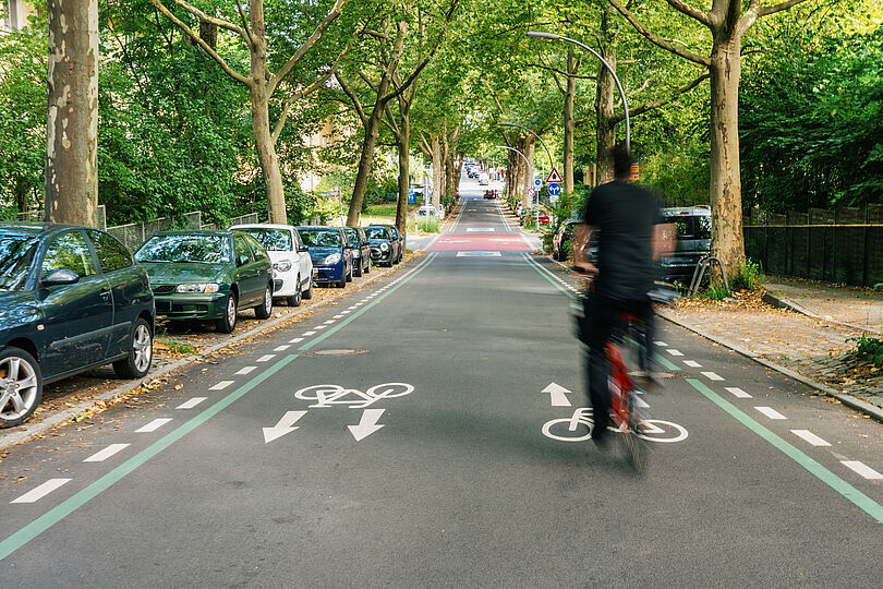 Fahrradfahrer fährt auf einer Fahrradstraße, die leicht abschüssig ist, auf eine kleine Kreuzung zu