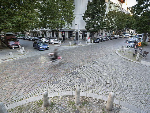 Blick von oben auf eine gepflasterte Straßenkreuzung in Prenzlauer Berg mit Auto- und Radverkehr