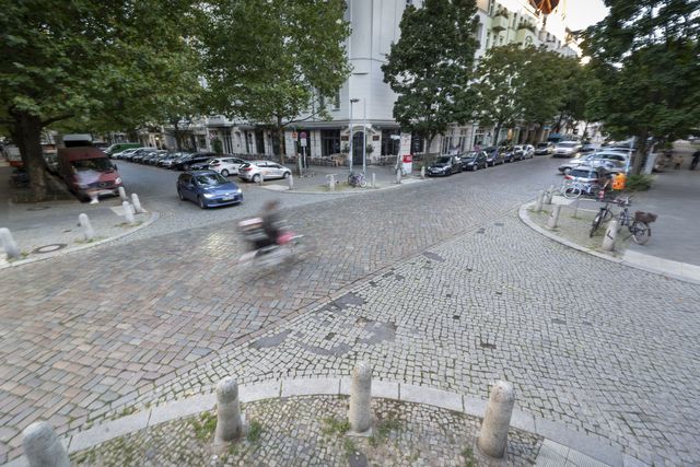 Blick von oben auf eine gepflasterte Straßenkreuzung in Prenzlauer Berg mit Auto- und Radverkehr