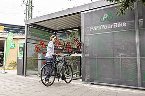 Eine Frau parkt ihr Fahrrad in einer gesicherten Sammelschließanlage am S-Bahnhof.
