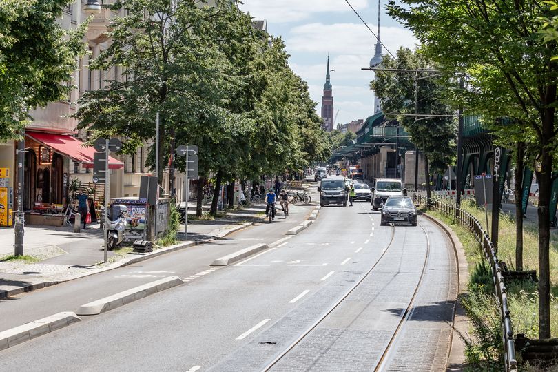 Radfahrstreifen auf der Schönhauser Allee, geschützt durch Betonborde. Daneben fahren Autos auf zwei weiteren Fahrspuren.