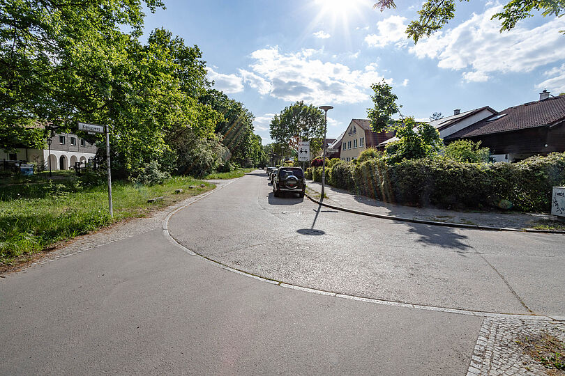 Asphaltierter Straße in einem Wohngebiet. mit parkenden Autos auf der rechten Straßenseite.