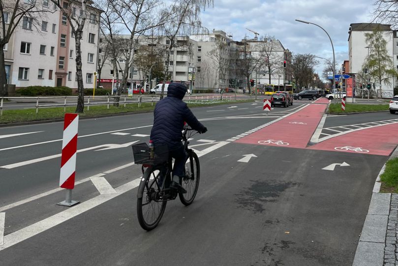 Radfahrender auf Radfahrstreifen vor einer Kreuzung mit zwei abzweigenden rotmarkierten Radfahrstreifen.