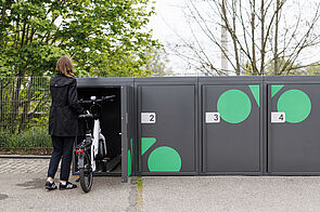 Frau schiebt ein e-Bike in eine Fahrradbox hinein