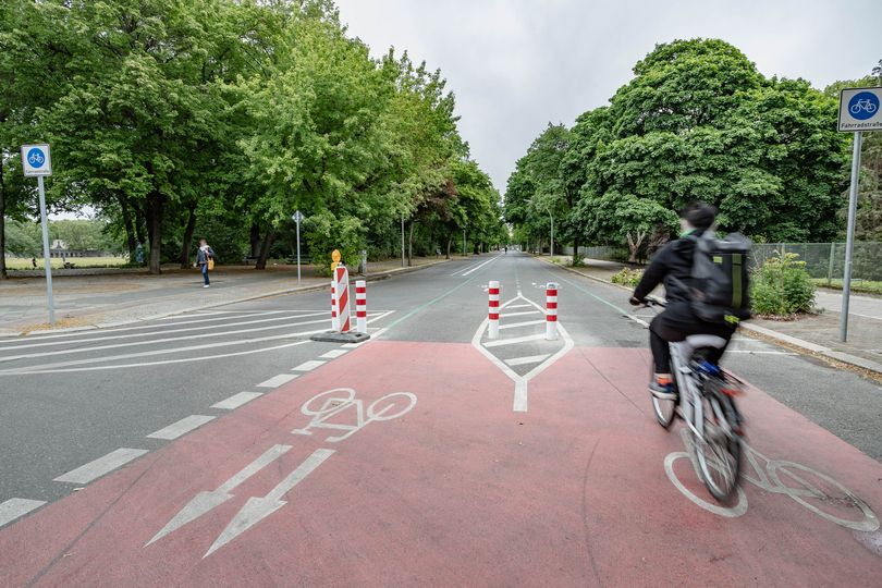 Radfahrende auf einer Fahrradstraße mit Rotmarkierung, Piktogrammen und Pollern im Kreuzungsbereich.